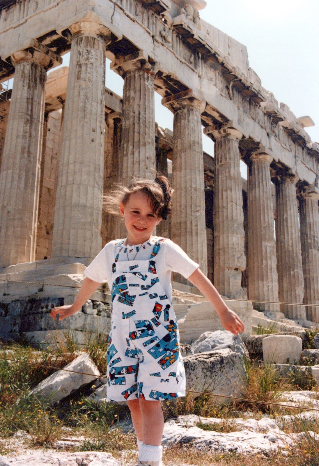A young girl in Mickey Mouse overalls spinning in front of the Parthenon columns